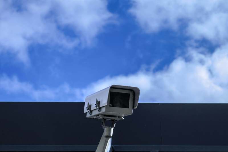 Photo of blogger holding compact security camera while checking live feed on smartphone outdoors at dusk